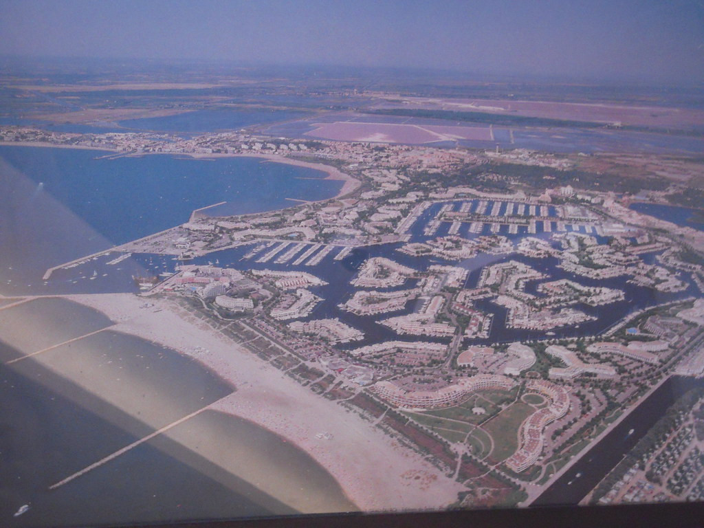 erial photograph showing a flat coastal landscape. At the center of it there is a marina, called Port Camargue and built in the Rhone Delta as part of a large-scale redevelopment plan of the French government in the 1960s. 